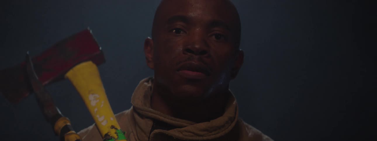 A man looks into the camera while holding two colorful axes