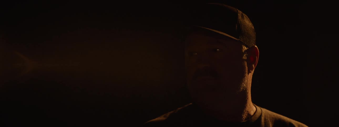 An officer on a stage turns 360 degrees to reveal his face wearing a baseball hat