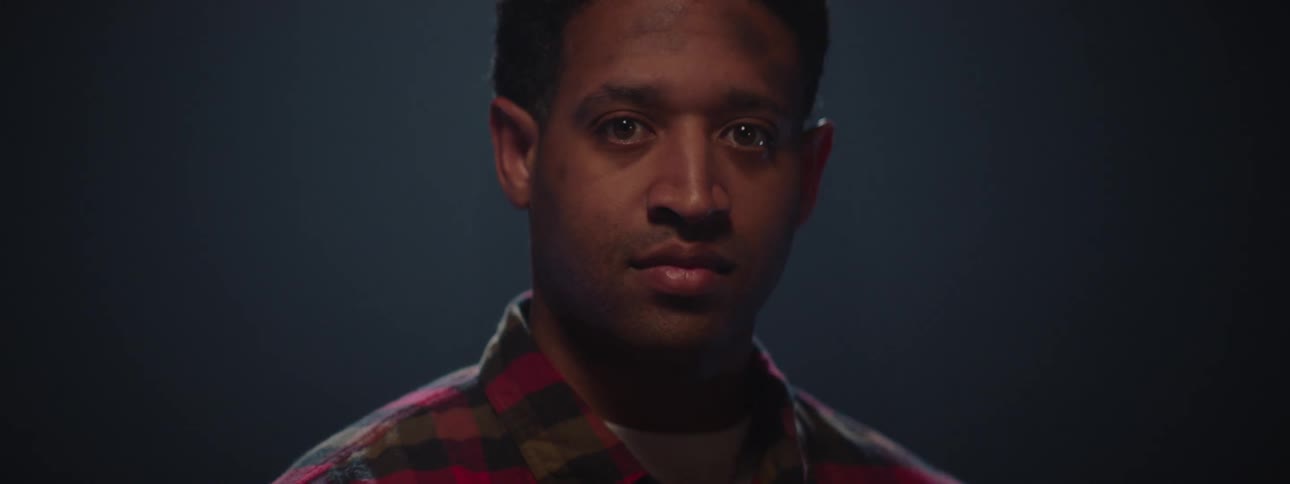 A sad black man stares forward in a dark area