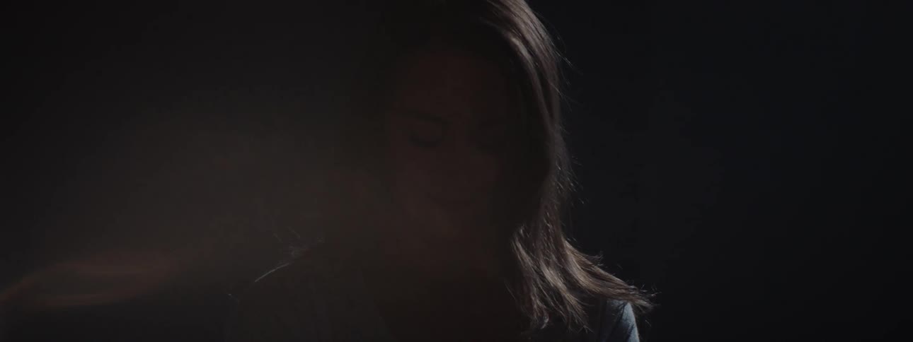 Light illuminates the face of a woman standing in the dark