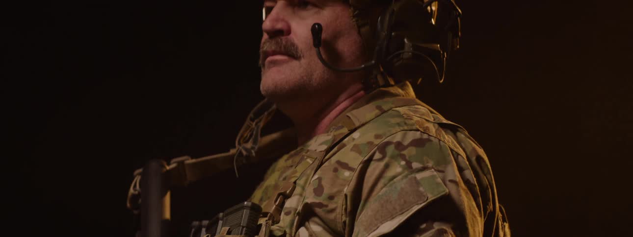 The video shows a person wearing militarystyle camouflage fatigues and holding a rifle the focus is on the upper torso and the rifle with a dark background suggesting an outdoor possibly tactical setting