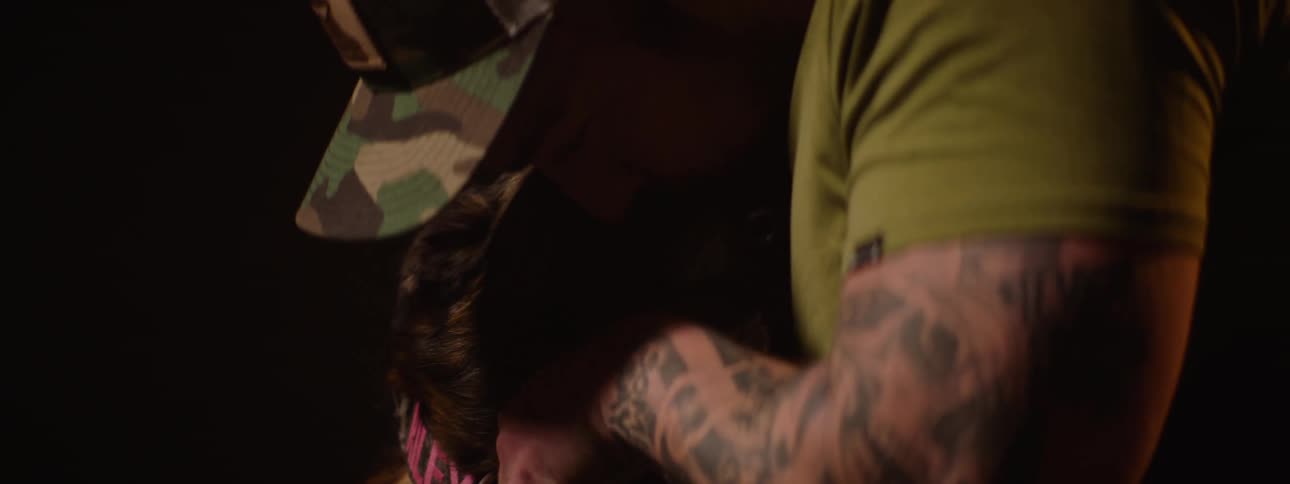 A military officer wearing an army uniform a hat and displaying tattooed arms is petting a canine