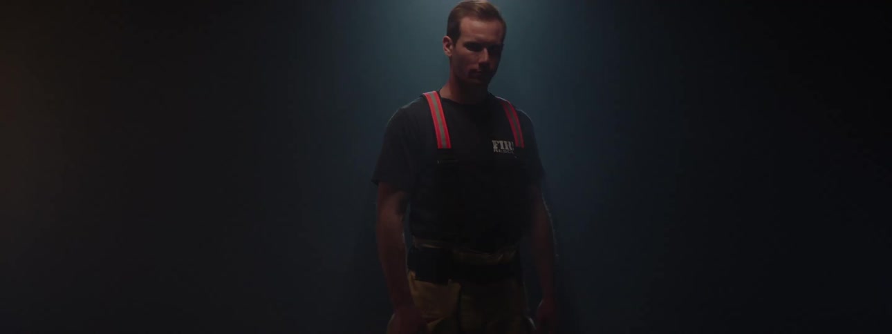 A male firefighter on a stage revealed by light as he spins 360 degrees