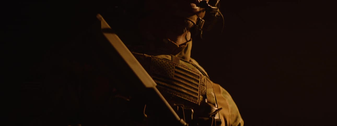 Close up of a black military man with full gear standing under yellow lighting at night