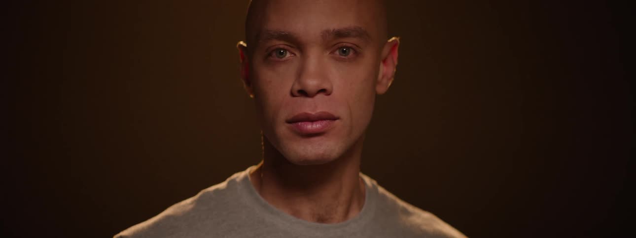 The face of a bald man who is doing well trying in the dark and a light is hitting his face