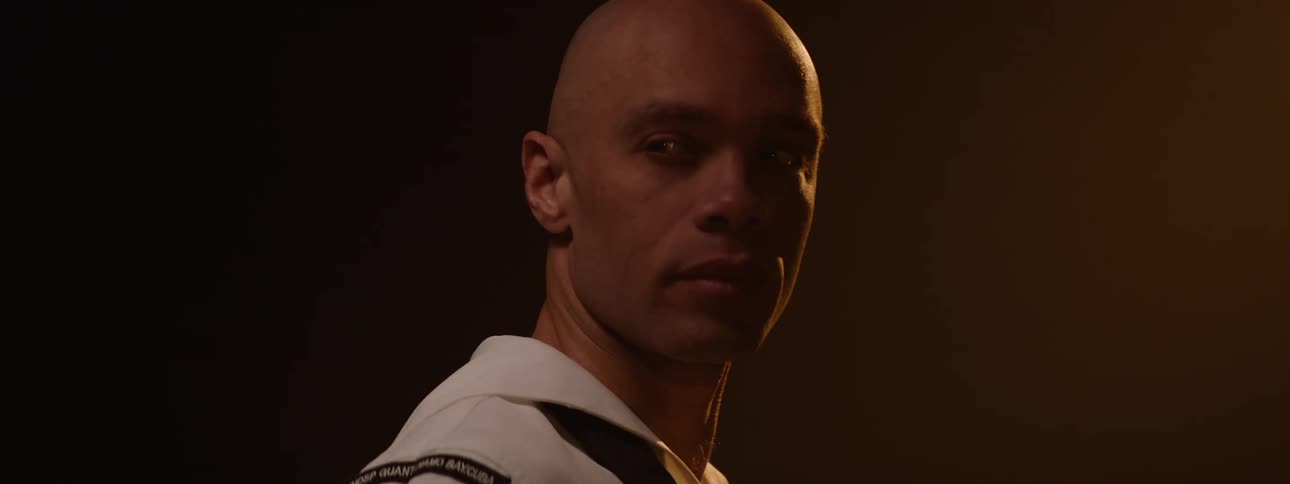Closeup portrait of a man with a shaved head wearing what appears to be a naval or formal uniform with a white collar