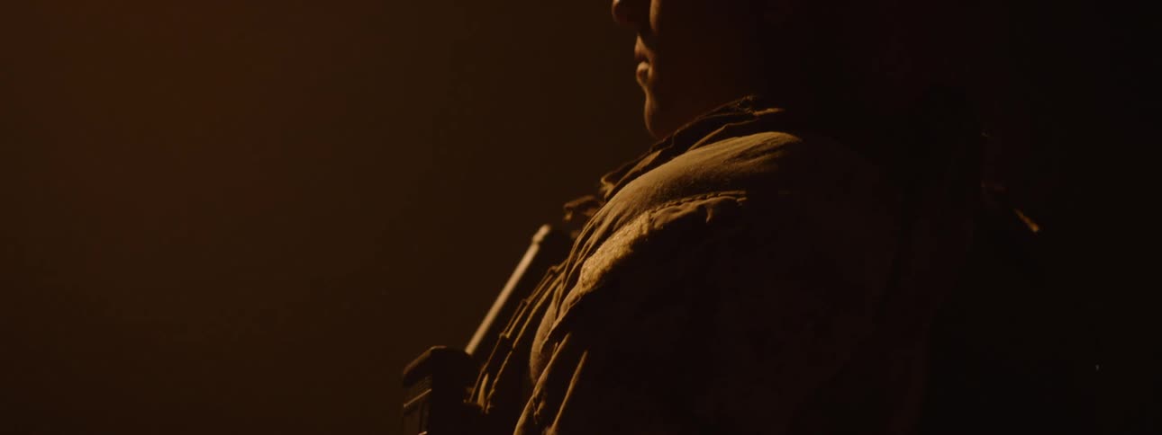 The face of a person wearing a cap who is in a dark room and holding a gun