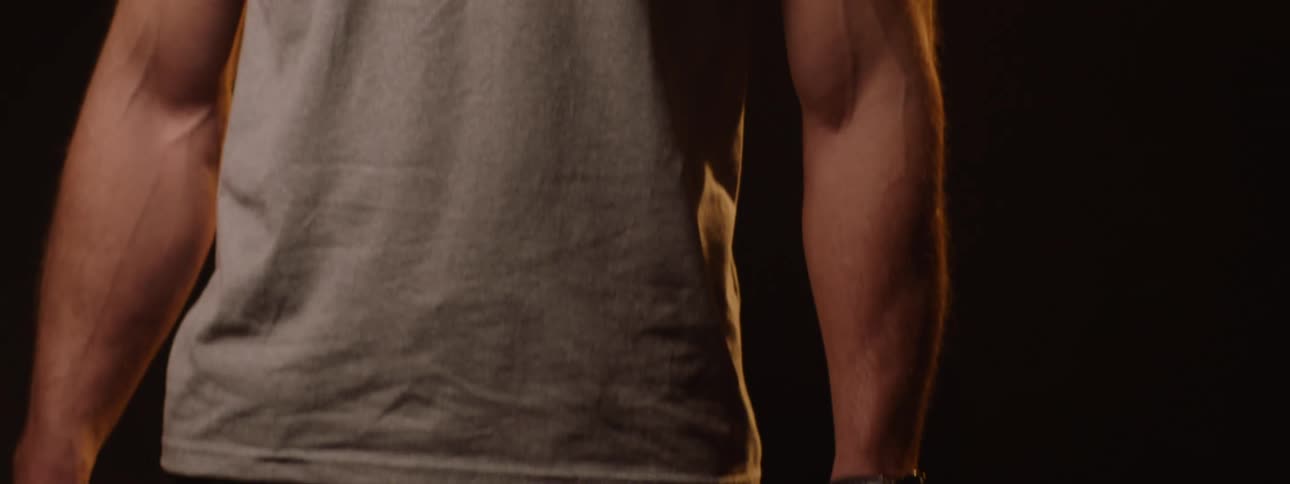 A bald man wearing an ashcolored tshirt and a wristwatch stands on a stage