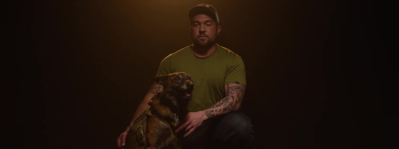 Man in a cap in a studiolit environment next to a dog in a military vest