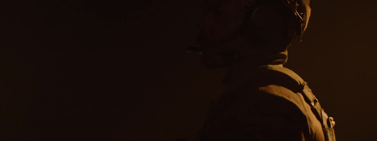 Light shining in a dimly lit area falls on a military man dressed in battle gear