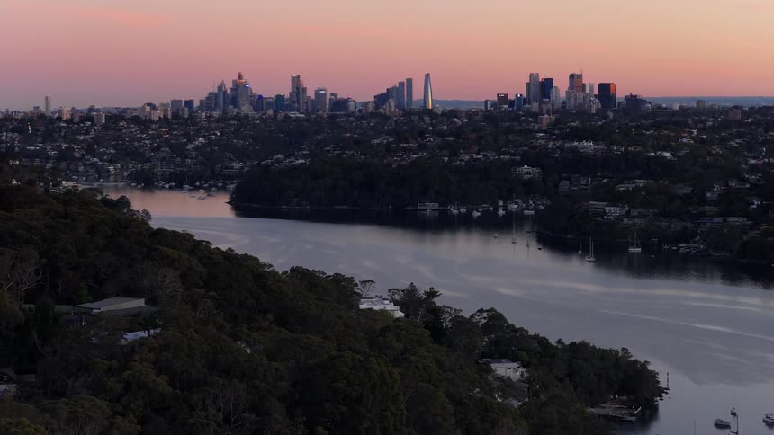 A calm cityscape at dusk with a river winding through forested hills