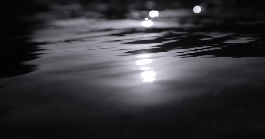 Eflections of light shimmer across the surface of dark rippling water in a closeup