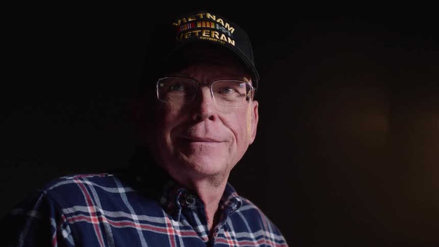 Elderly man wearing a cap and glasses with a happy expression in an indoor space