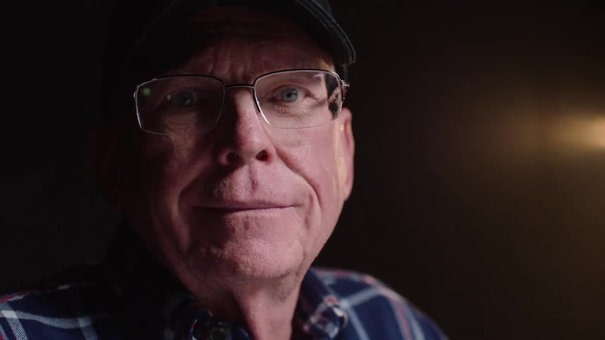Close up portrait of an elderly man wearing a black veteran face cap with glasses
