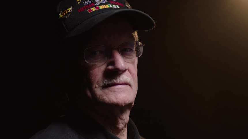 An elderly man standing on a stage wearing a hat and turning 360 degrees