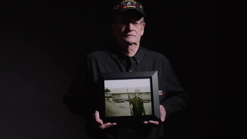 Elderly male veteran holding a framed picture of his military service days