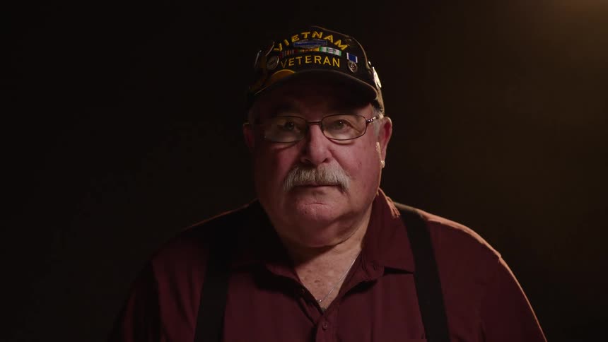 Man in cap and glasses with a white mustache in a space with studio lighting