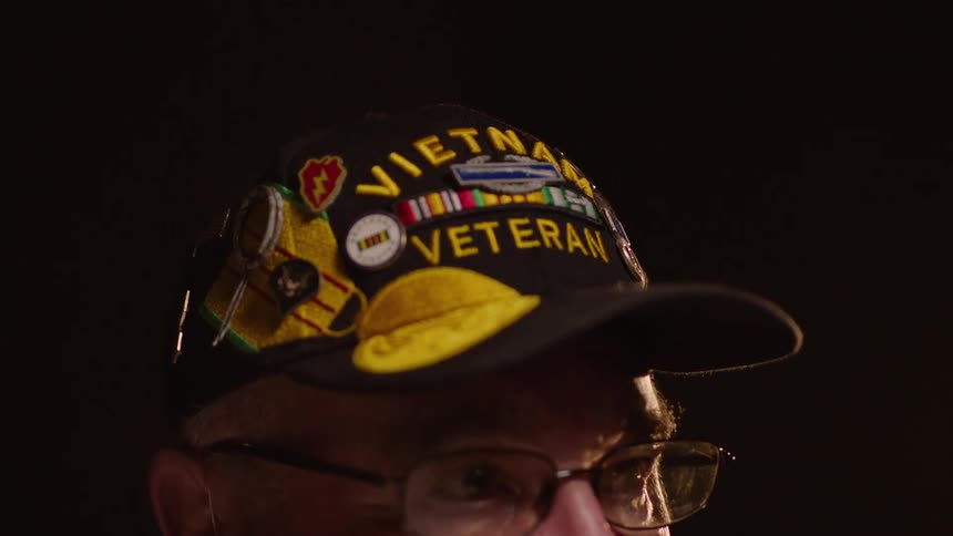 An elderly man wearing glasses and a hat that says vietnam veteran