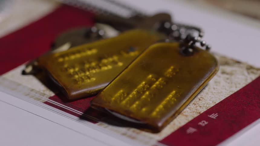 A closeup of two ambercolored military dog tags resting on a red and white printed page
