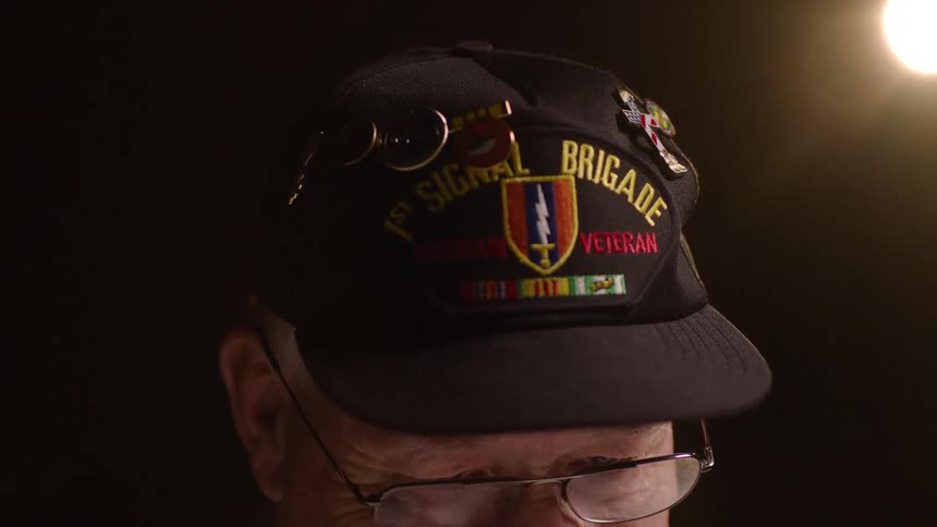 An elderly man wears a veterans hat
