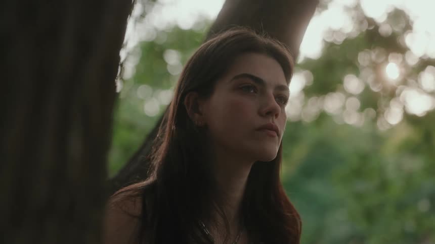 Close up portrait of a young woman standing outdoors under a tree during daytime