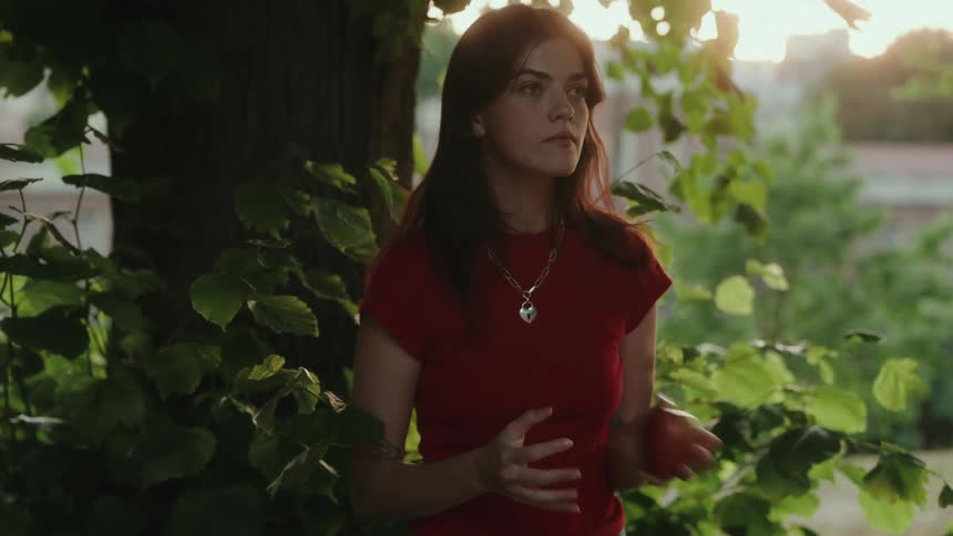 The girl tosses an apple between her hands under the tree