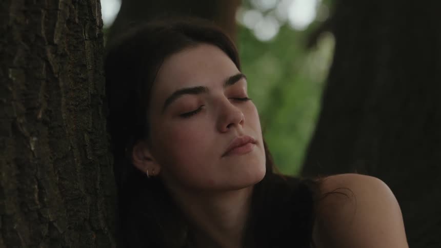 Woman with eyes closed leaning against a tree trunk