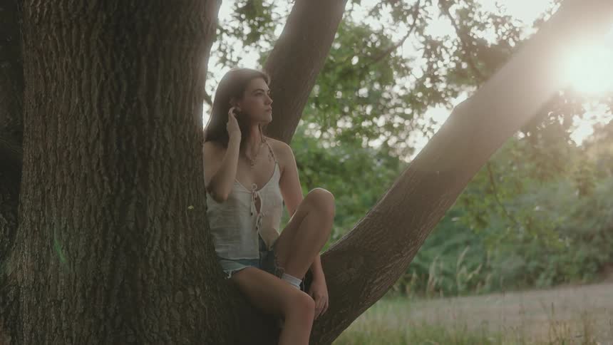 Young woman sits on a tree branch outdoors during daytime