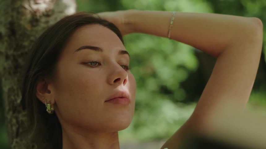 Pretty blue eyed woman with hoop earring and gold bracelet sit under a tree while reading a book woman looks peaceful and relaxed on a beautiful day