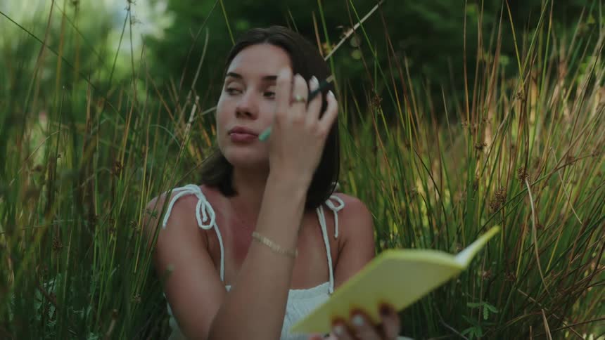 Woman in white dress sitting on grass outdoors and writing in a book