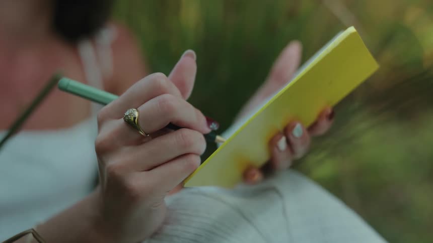 Hands of a seated woman writing in a notebook
