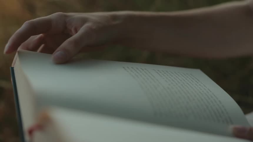 Close up of a woman flipping through a book pages while reading outdoors during daytime