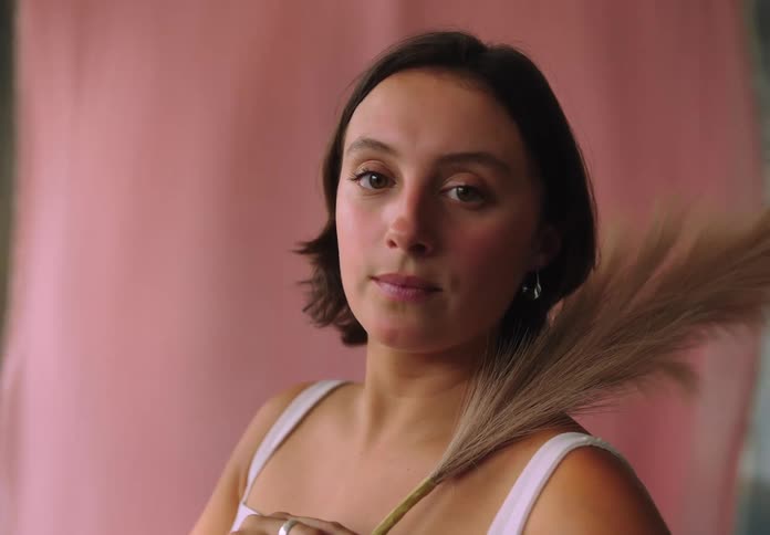 A young woman smiles and poses confidently in front of a pink background