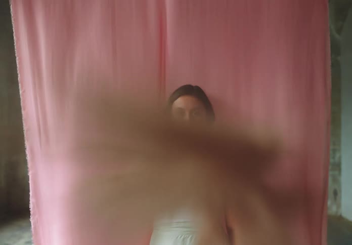 A woman playfully covers the camera with a fuzzy object in front of a pink backdrop