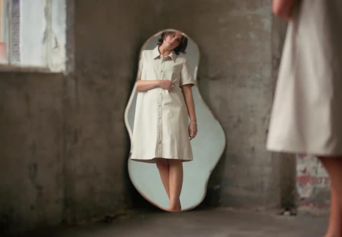 Woman stands before curvy mirror gazing at her reflection