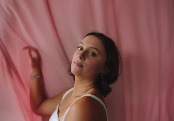 Woman poses confidently with one arm raised against a pink backdrop