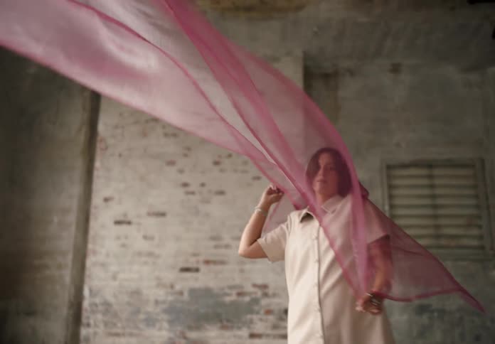 A young woman playfully holding a curtain and dancing with it at midday