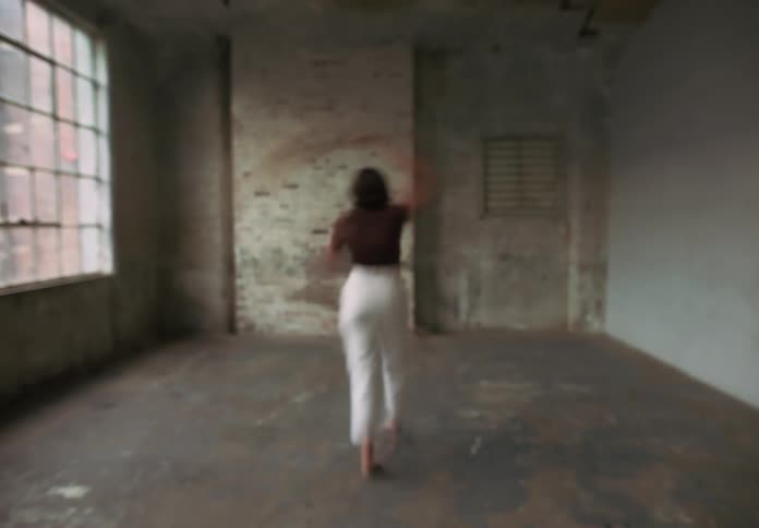 Fullbody shot of a women dancing with dried plant in her hands in a concrete room