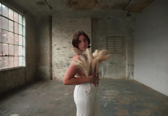 Woman models a feather grass decorated blouse while standing in an empty room during the daytime