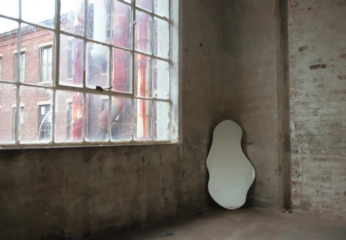 Woman in a dress walking through a bare room with a mirror in the background