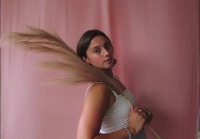Woman poses with pampas grass in front of pink backdrop