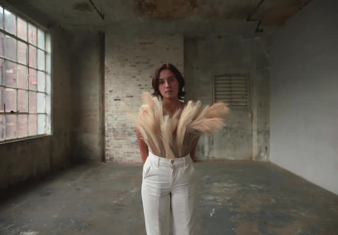 Young woman in white pants and reed plants around her waist covering her bust
