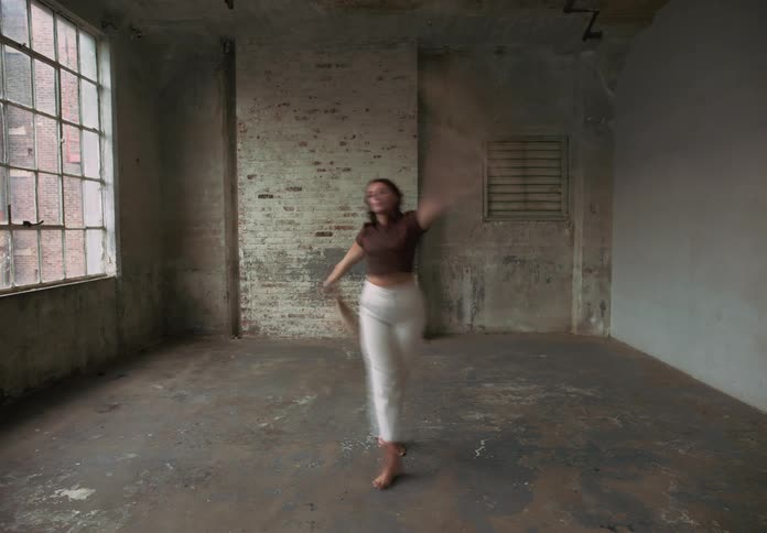 Fullbody shot of a person standing barefoot in the center of a room dancing with dried plants in her hands