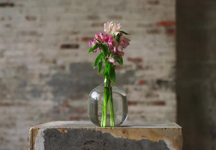 Pink and white flowers inside a vase with clear water on a wooden surface