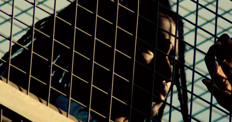 Dreadlocked man seen through a metal fence