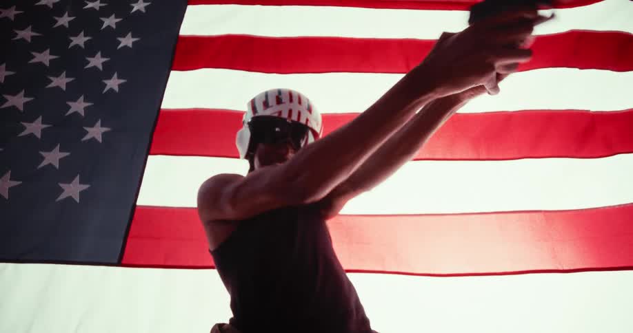 A man stands in front of a flag and shoots a gun