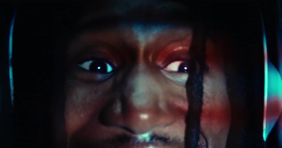 The video features an extreme closeup of a persons face with their eyes wide open and reflecting blue light their expression shifts from intense to a brief moment of apparent distress or fear revealing teeth before returning to a more fixed stare