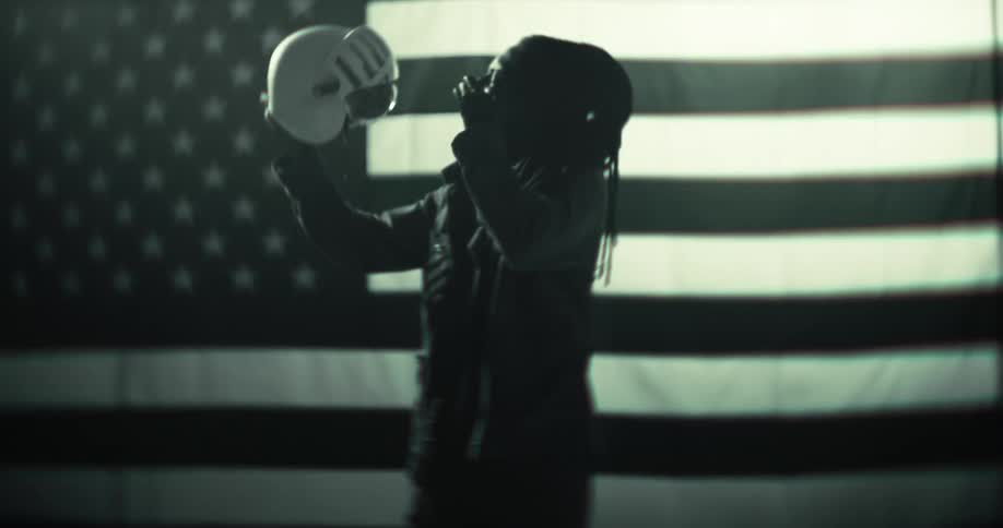 The woman is holding up a helmet in front of an american flag