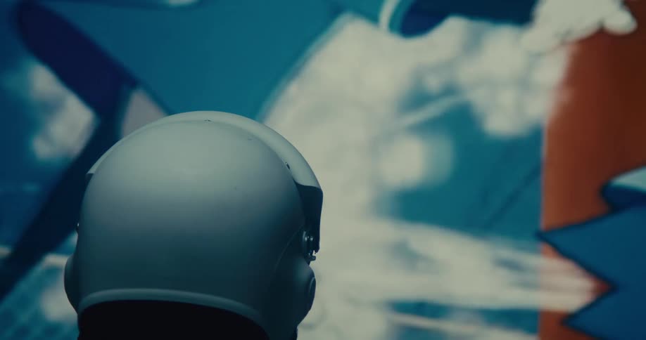 The video shows the back of a lightcolored helmet with projections or screens displaying various dynamic visuals in the background these visuals include abstract patterns colors and possibly distorted human figures creating a futuristic