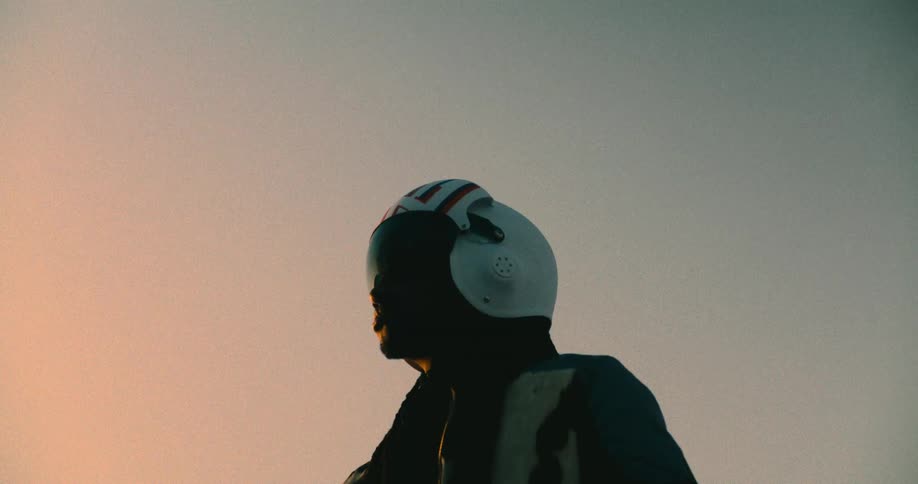 The video features a person in silhouette against a clear sky with a warm glow on the left side suggesting a sunset or sunrise they are seen placing a white helmet with red and blue stripes onto their head